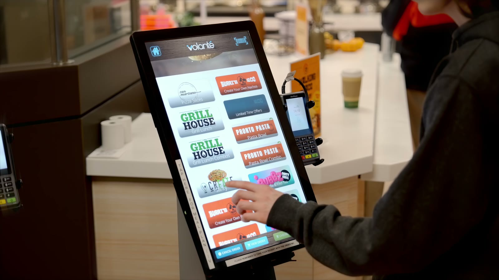 A student ordering at a self-serve kiosk showing Grill House, Pronto Pasta, Create, Bubbz and Burrito Loco